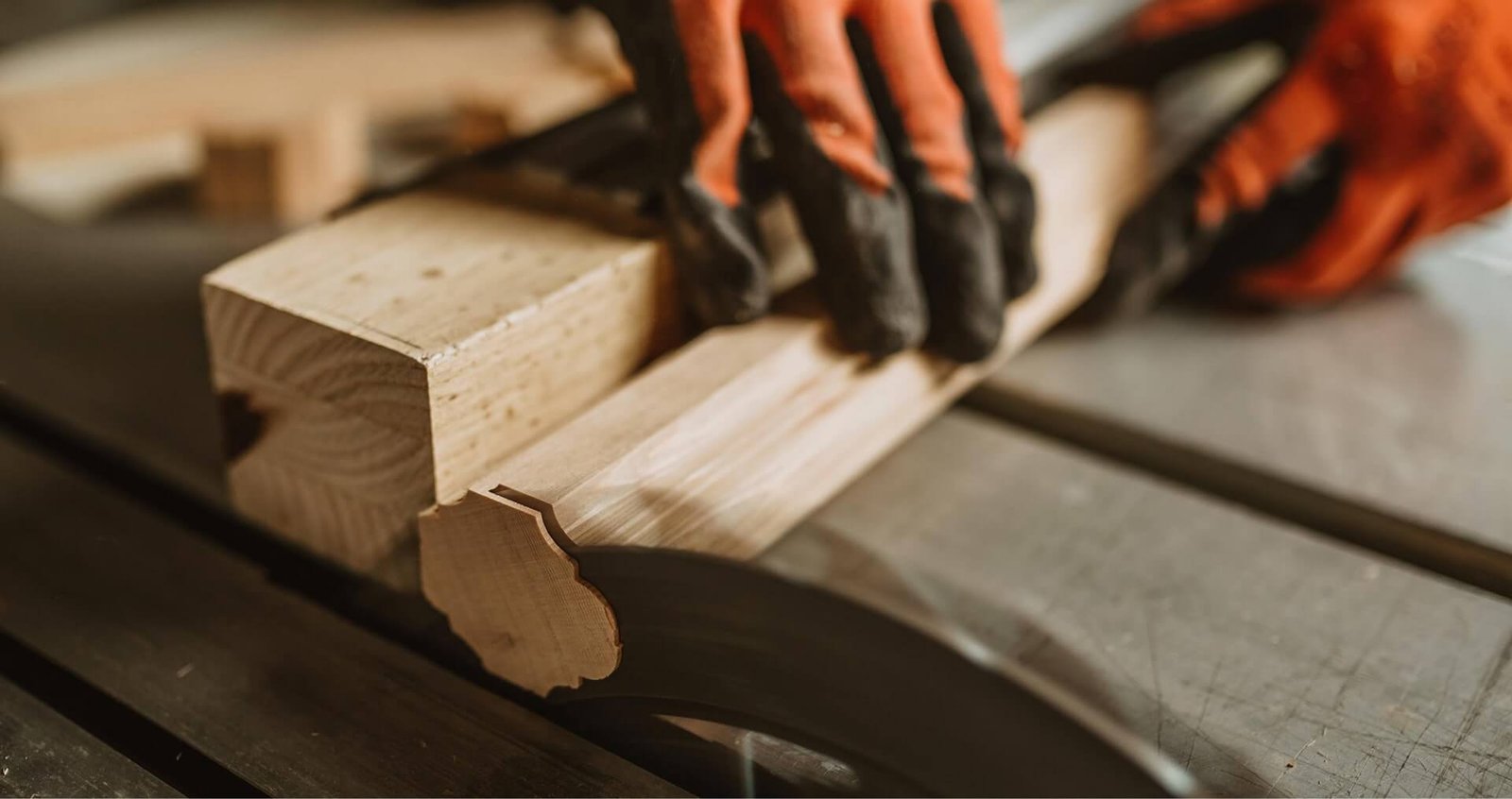 Close-up of gloved hands using a table saw to cut a piece of wood