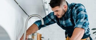 Professional handyman leaning over to inspect or repair a kitchen sink