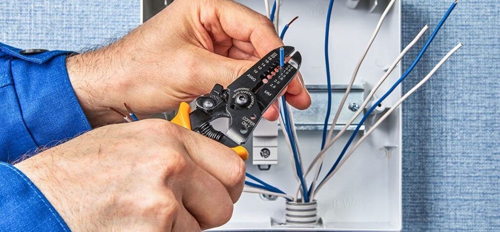 Electrician stripping wire insulation inside a junction box