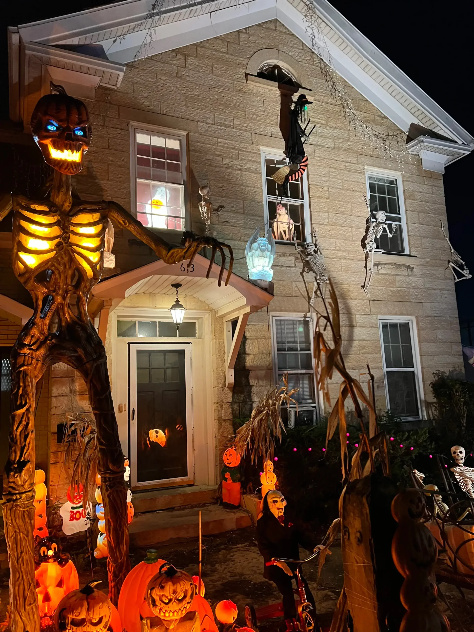 Elaborate haunted house exterior featuring a giant pumpkin skeleton, climbing ghouls, and illuminated props by Halloween Decorating Service Chicago.