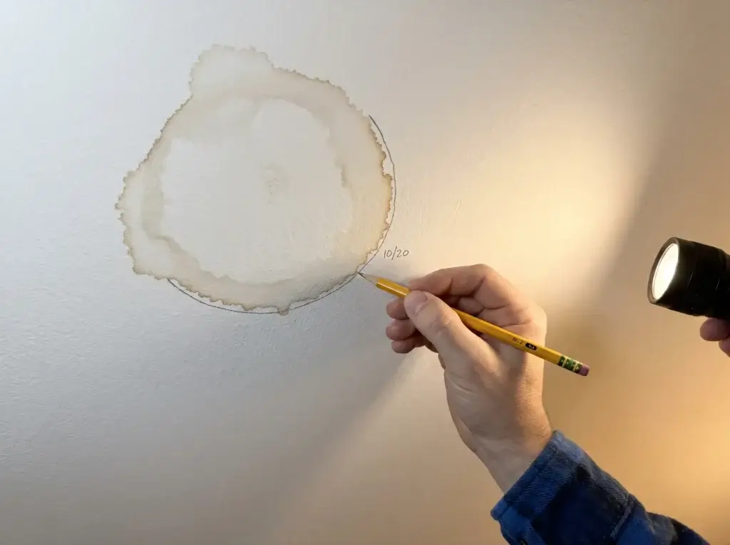 Pencil line and date marked around a brown stain on ceiling to tell an old stain from an active leak